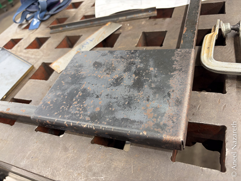 A corner made of steel bar. A piece of sheet metal has been folded, and the folded edges cover the bar